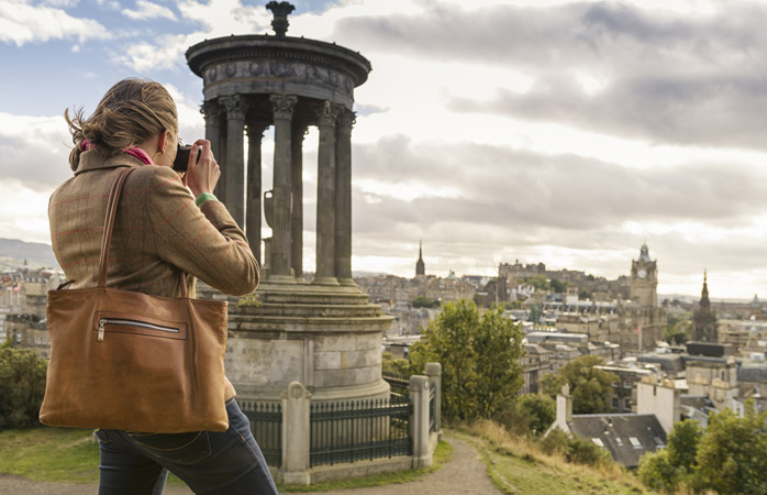 A woman takes a photo of Edinburgh from Calton Hill