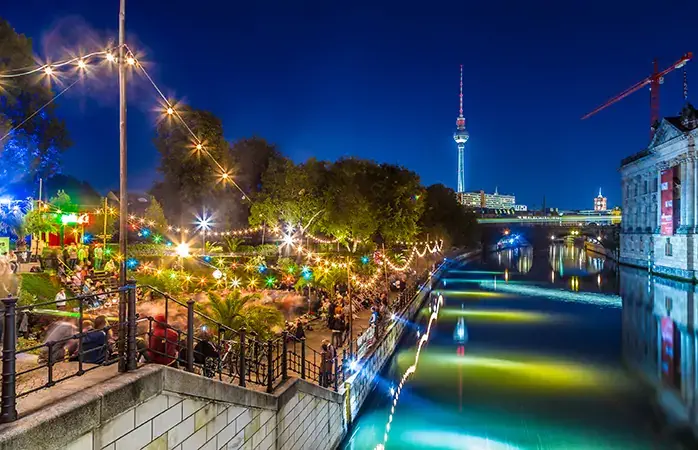 People dancing at summer Strandbar beach party near Spree river at historic Museum Island with famous TV tower in the background in twilight during blue hour at dusk, Berlin Mitte district, Germany; Shutterstock ID 377514604