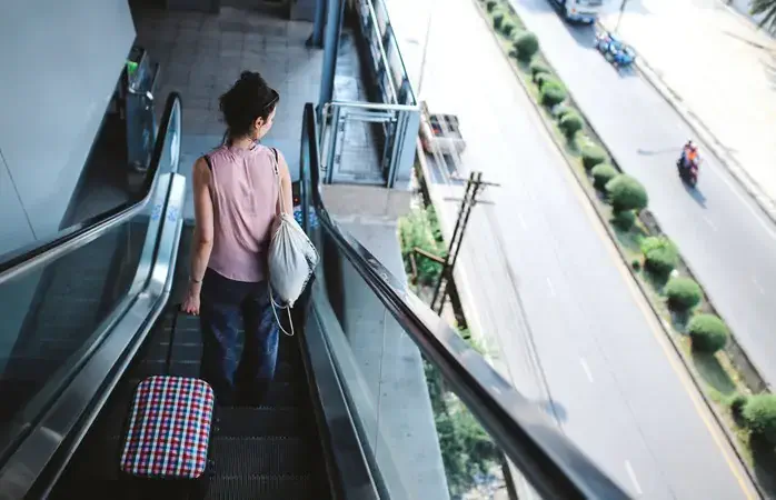 Image of a young woman with a suitcase traveling solo, getting off at the Bangkok sky train station in the morning.