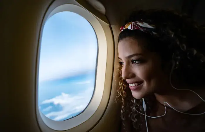 Portrait of a happy woman traveling by airplane and listening to music with headphones while looking through the window - lifestyle concepts